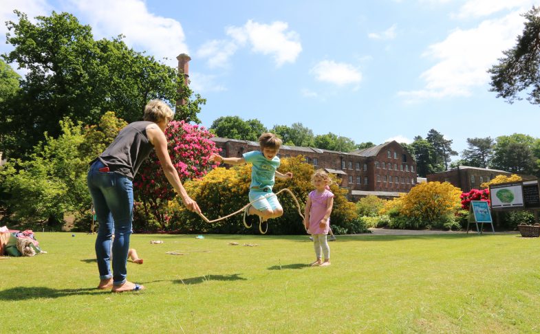 Two small children and their guardian have fun skipping in a large garden.