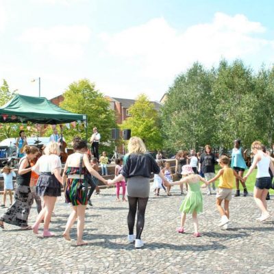 People dance in a circle in Hulme Park