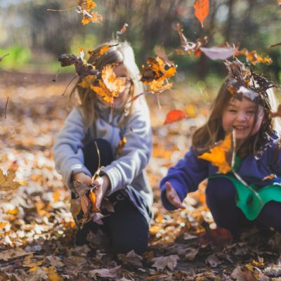 Two young children have fun throwing leaves up into the air.