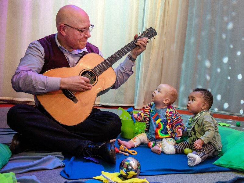 A man plays a guitar and sings to two small children