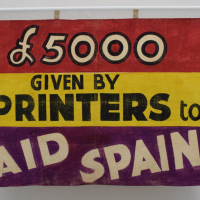 A banner which says "£5000 given by printers to aid Spain".