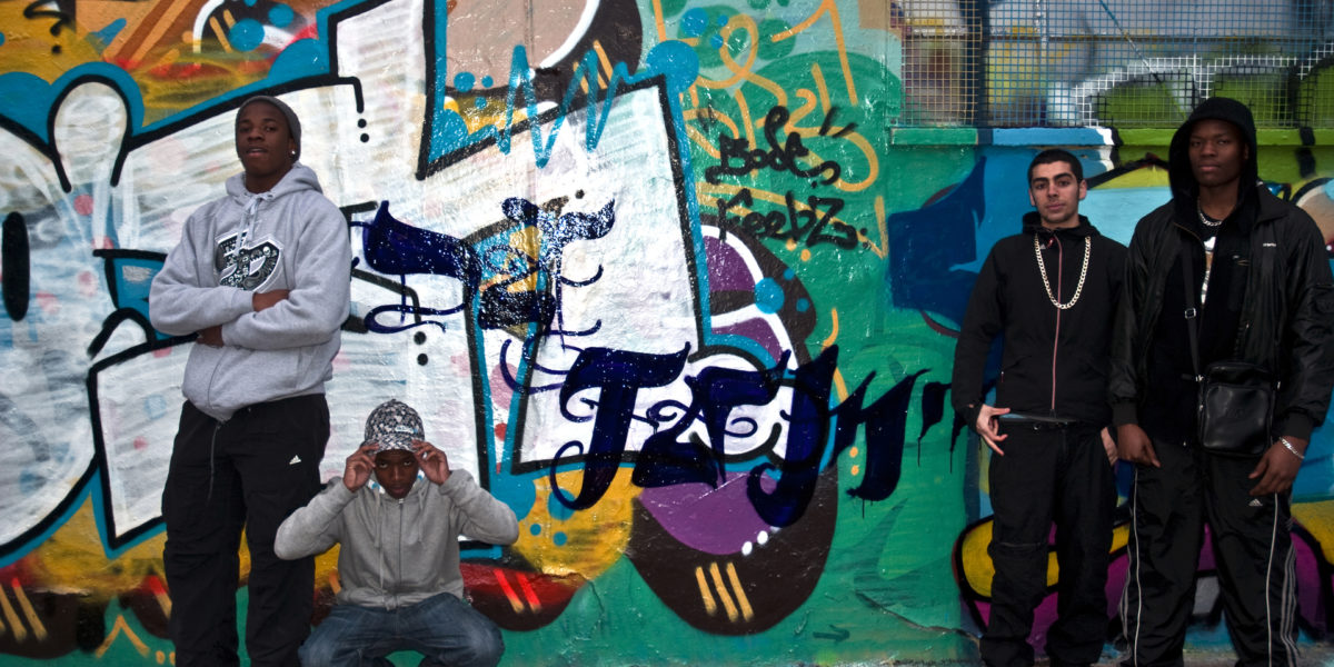 Members of the M13 Youth Project stand in front of a wall painted with some street art.