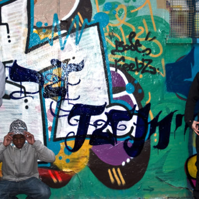 Members of the M13 Youth Project stand in front of a wall painted with some street art.