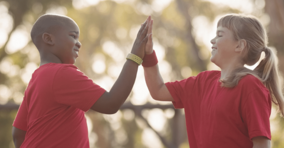 A boy and girl, both wearing red t-shirts, high-five eachother.