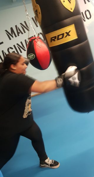 A young person wearin boxing gloves pounds a punching bag.