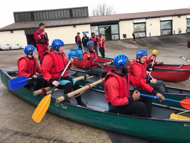 A group of young people sit inside canoes on the jetty at Debdale Outdoor Centre as they learn about sailing.