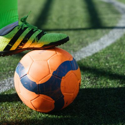 A footballer traps a ball under their foot.