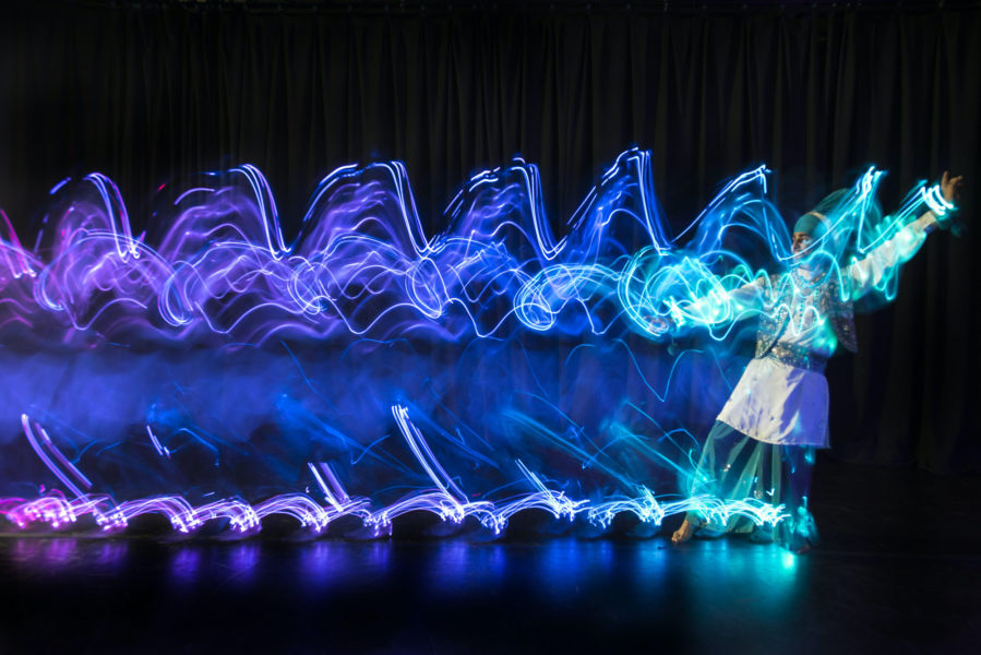A dancer moves across the stage in a colourful show of lights.