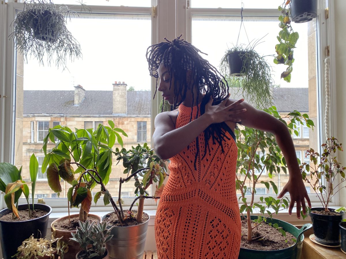 A lady wearing a bright ornage dress dances in front of her window.