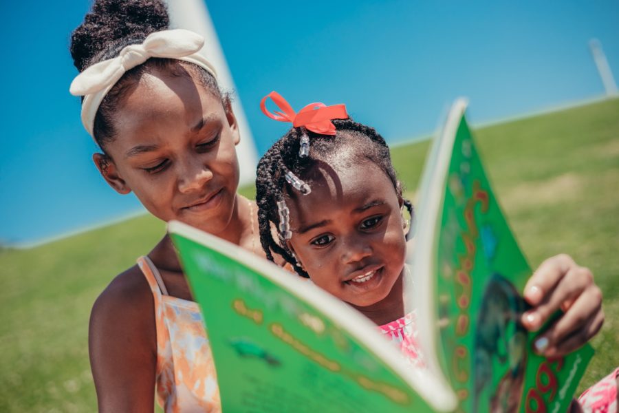 An adult and a child read a book together outside.