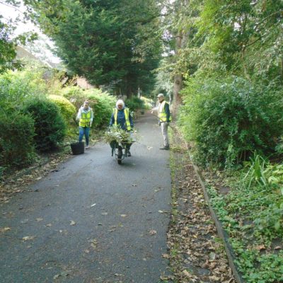 A group of volunteers wearing hi-vis vests clean up a park pathway.
