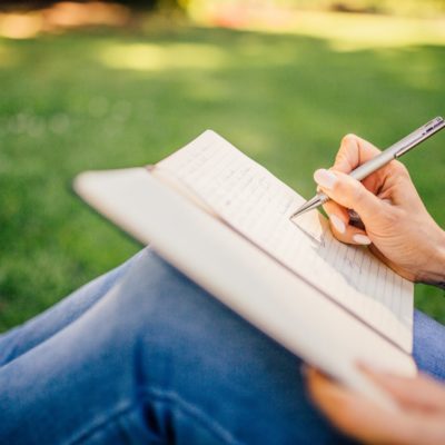 A person sits outside on the grass and writes in a note book.