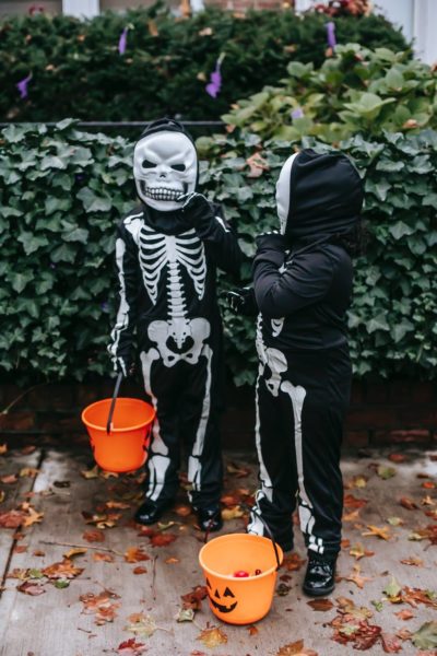 Two children, dressed up as skeletons, carry pumpkin trick or treat buckets.
