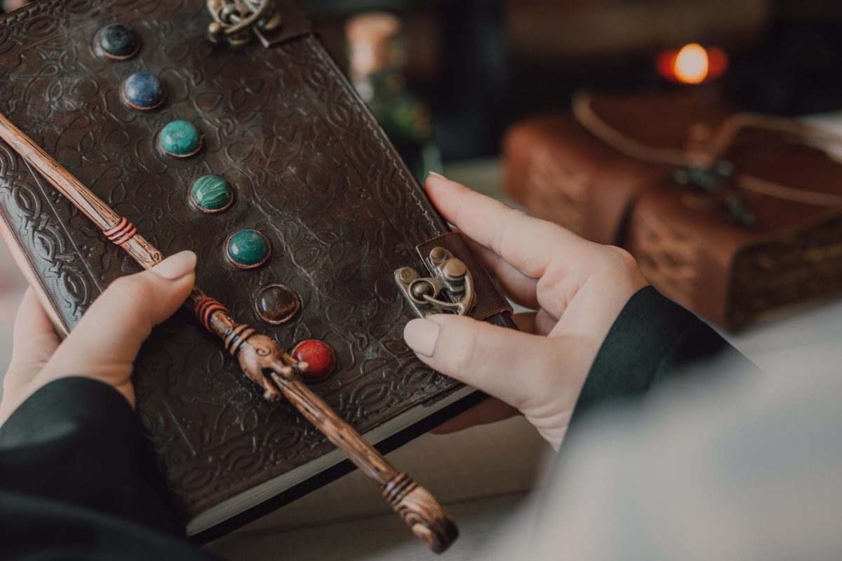 A person holds a spell book and a magic wand