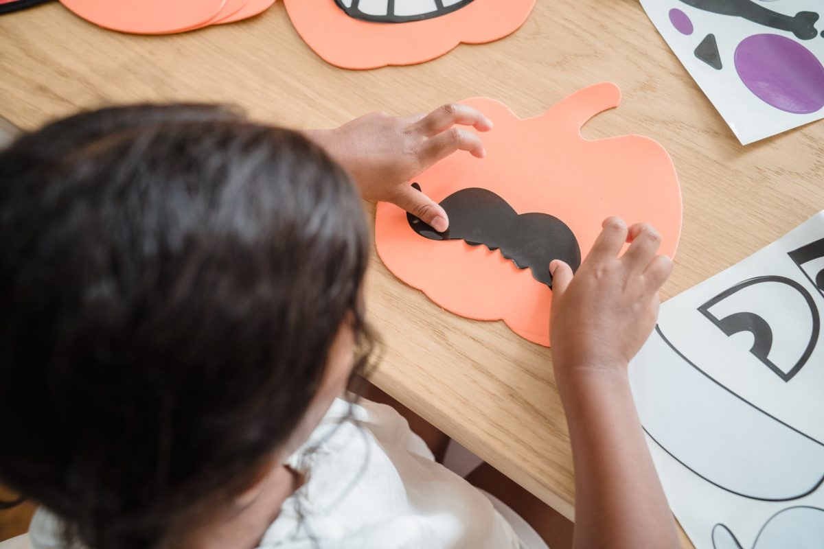 A small child sits at a table doing Halloween craft activities.