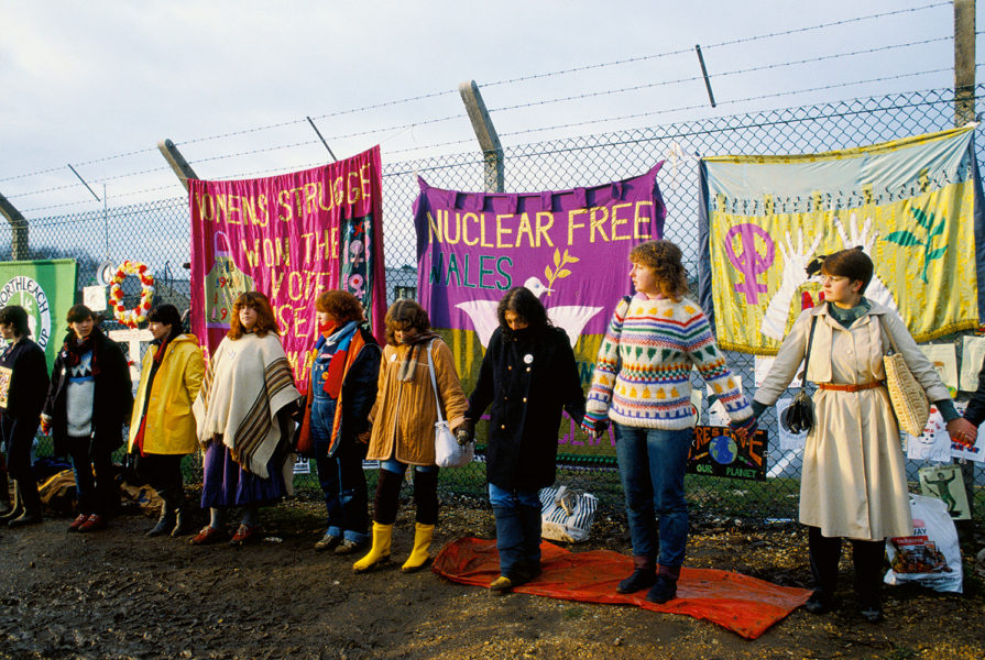 Womens Peace Camp protestors holding hands encircling USAF Base perimeter fence where three banners hang behind