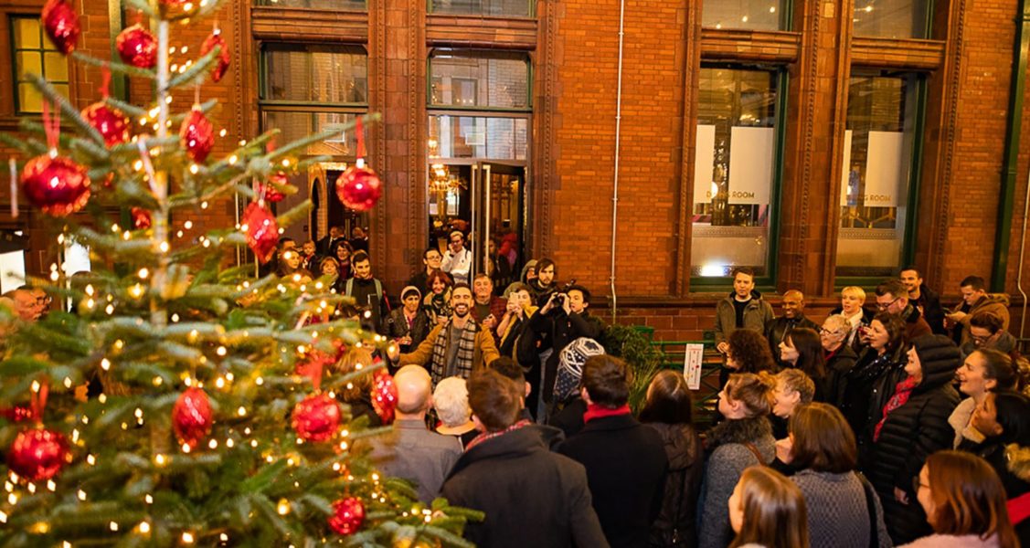 A crowd of people gather by a large, decorated Christmas tree outside.