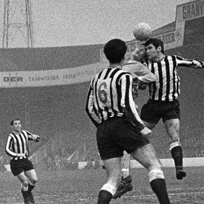 Two footballers from opposing teams jump to head the ball. The team were black and white striped kits.