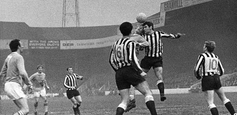 Two footballers from opposing teams jump to head the ball. The team were black and white striped kits.