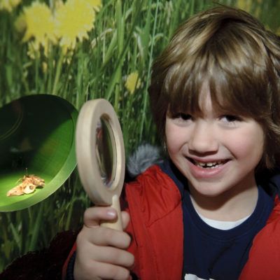 A child in a red gilet holds a magnifying glass