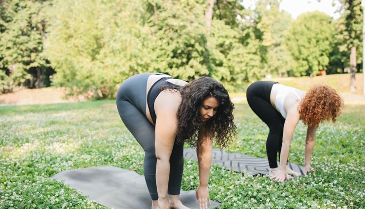 Two people stand holding their ankles for a yoga session outside