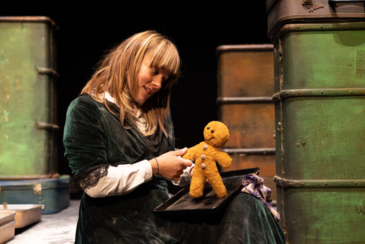 A person sits with a green dress on and holds a Gingerbread Man puppet.
