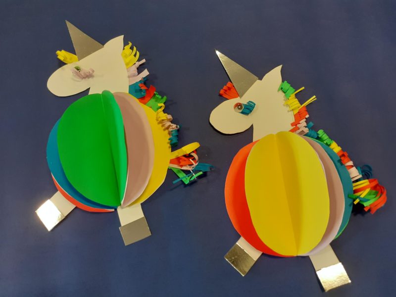 Two rainbow unicorns that have been crafted from coloured paper.
