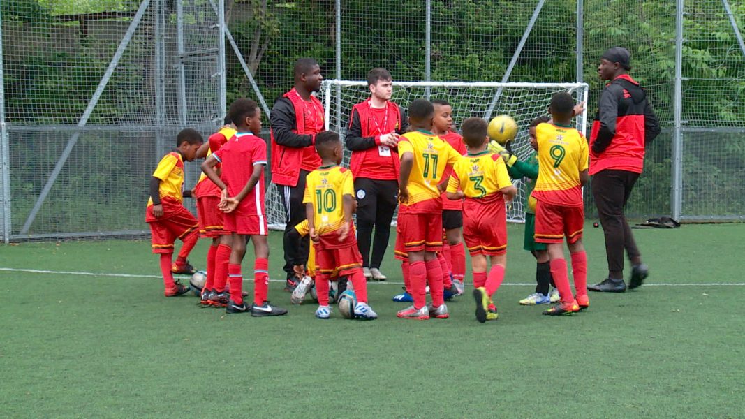 A children's football team stand on a football pitch