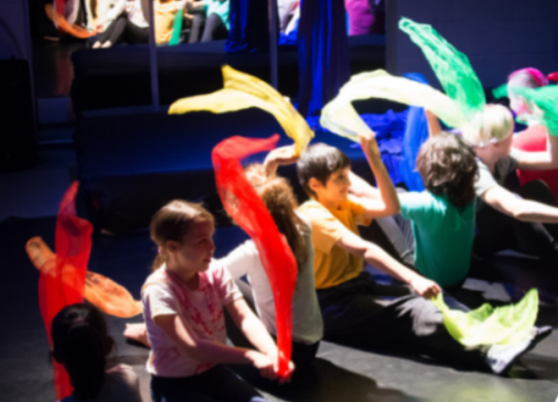 Children sat on the floor in a line waving colourful pieces of fabric above their heads