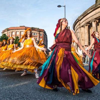 Dancers from Global Grooves wearing long red and orange coloured dresses perform outside