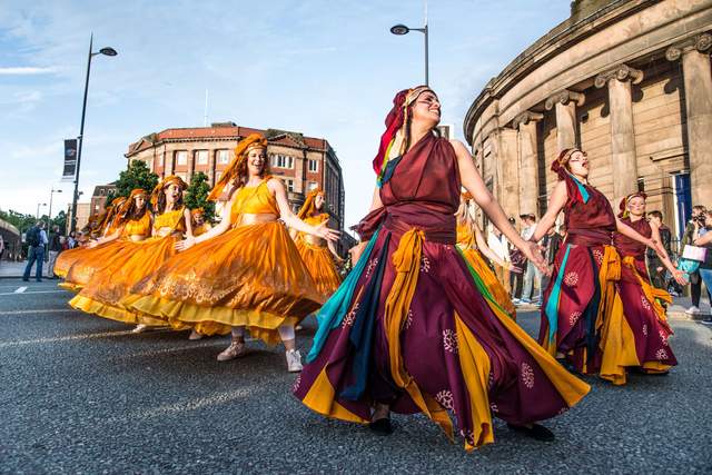 Dancers from Global Grooves wearing long red and orange coloured dresses perform outside